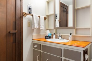 A bathroom with a wooden door, a white sink, and a mirror above it. There are towels hanging on a rack and toiletries on the counter. - Outpost: Teton Shadows Rimrock C (Jackson)