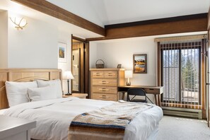 A bedroom with a large bed, a desk, a chair, a dresser, and a window with a view of trees and mountains. - Outpost: Teton Shadows Rimrock C (Jackson)