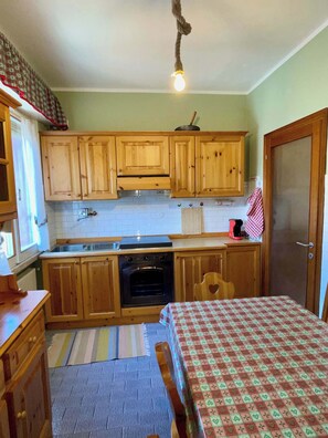 A compact kitchen with wooden cabinets, a stove, and a single hanging light bulb.