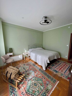 A bedroom with a bed, a chair, a desk, and a patterned rug.