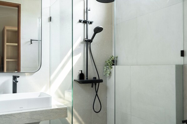 Un baño moderno con cabina de ducha de vidrio, un lavabo blanco y un espejo.