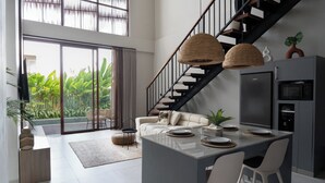 A modern kitchen with a central island, a dining area with chairs, a staircase, and a view of greenery outside. - Lulu Villa - 2-bedrooms villa in Canggu (Canggu)