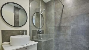 A modern bathroom with a round mirror, a white sink, and a glass-enclosed shower. - Charming apartment Center of Paris-Montmartre (Paris)