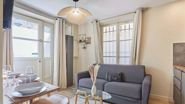 A modern living room with a grey sofa, a glass coffee table, and a dining table set with plates and glasses. - Charming apartment Center of Paris-Montmartre (Paris)