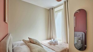 A hotel room with a bed, pillows, a small table with towels, a window with curtains, and a mirror on the wall. - Charming apartment Center of Paris-Montmartre (Paris)