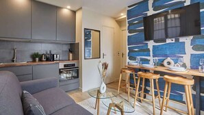A modern kitchen with grey cabinets, a built-in oven, and a dining area with stools and a TV mounted on the wall. - Charming apartment Center of Paris-Montmartre (Paris)
