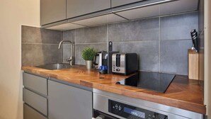 A modern kitchen with grey cabinets, a stainless steel sink, a wooden countertop, and a built-in dishwasher. - Charming apartment Center of Paris-Montmartre (Paris)