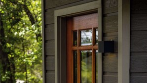 Uma porta de madeira com uma janela, uma pequena luminária externa e um deck de madeira.