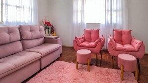 Una sala de estar con un sofá rosa, dos sillones rosa y un otoman a juego.