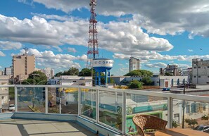 A rooftop terrace with glass railings, a blue water tower, and a cityscape in the background.