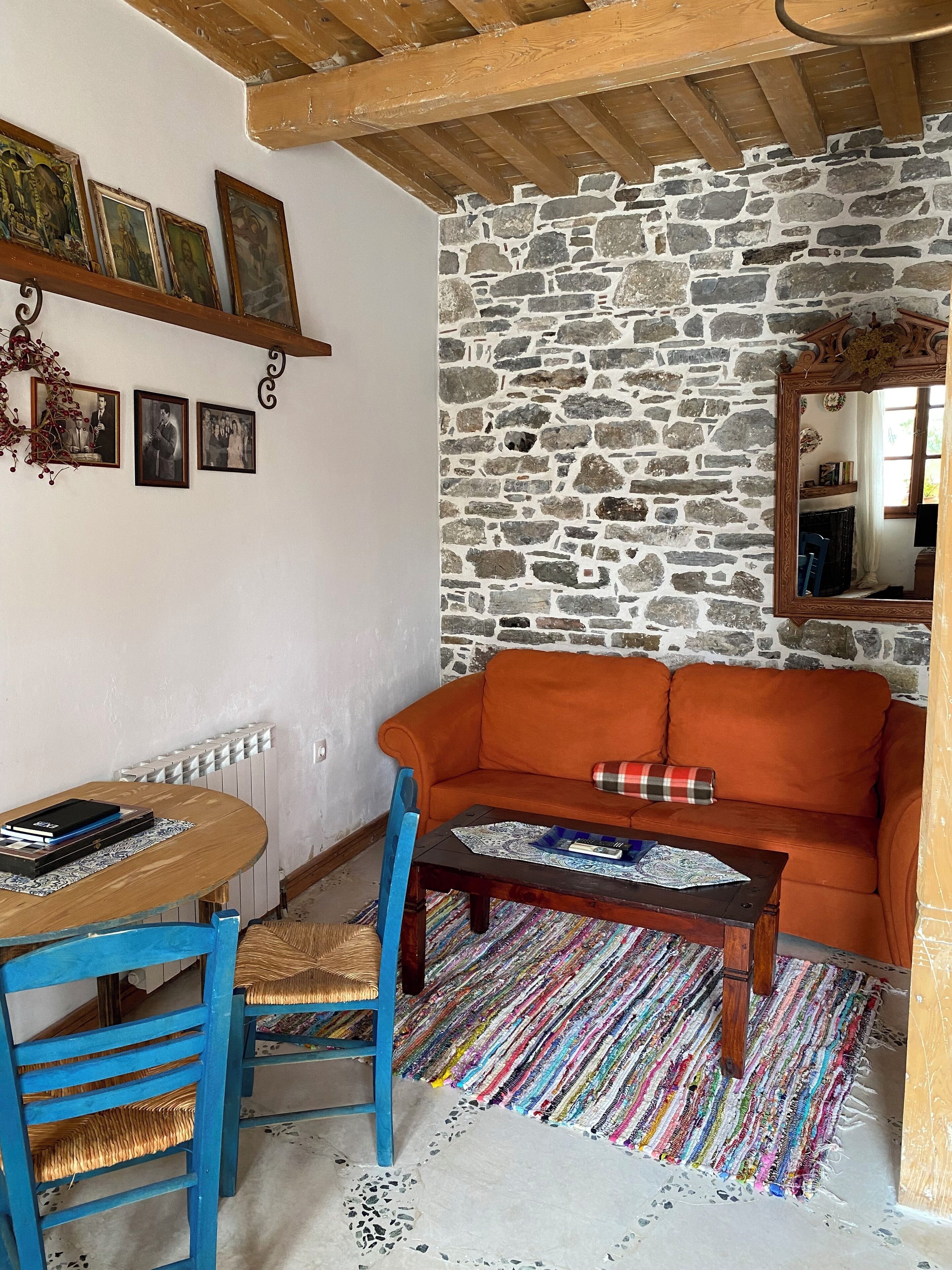 A cozy living room with a stone wall, a wooden ceiling, a blue chair, an orange sofa, and a coffee table.