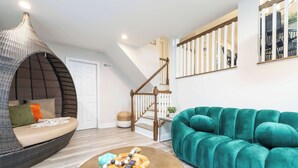 Een woonkamer met een blauwgroene bank, een rieten fauteuil en een houten salontafel met een afstandsbediening.