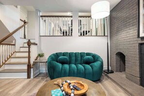 A modern living room with a green velvet sofa, a wooden coffee table with a remote control, and a staircase with wooden railings.