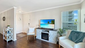 A living room with a TV, white furniture, a fireplace, and a large window with blinds. - $400 Free Activities, Pool, Pickle Ball, Tennis, Fitness Area! (Gulf Shores)