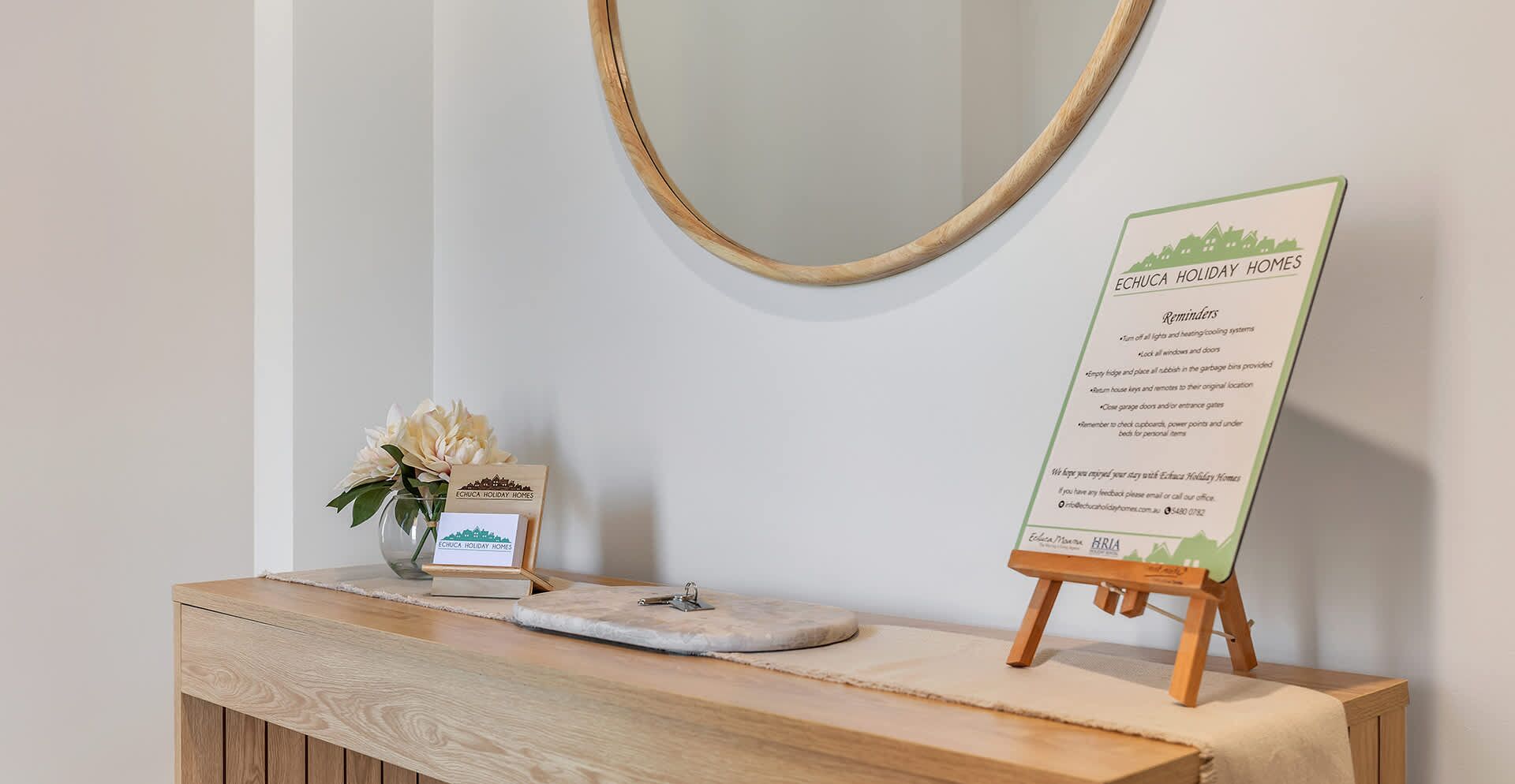 Un comptoir d’accueil en bois, agrémenté d’un panneau indiquant des informations importantes pour les clients, d’un vase avec des fleurs et d’un miroir au-dessus.