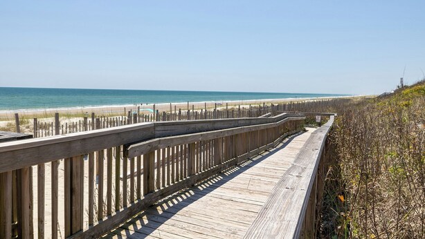 A wooden boardwalk leading to a beach with a clear view of the ocean.