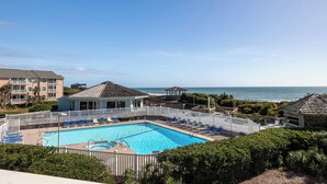 A pool area with a view of the ocean, surrounded by a white fence and lounge chairs.