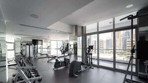 Un gimnasio moderno con diversos equipos de ejercicio, amplias ventanas que ofrecen vistas a la ciudad y un espacio amplio.