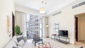 Una sala de estar moderna con un sofá, una mesa de centro de vidrio, un televisor y un ventanal con vistas a rascacielos.