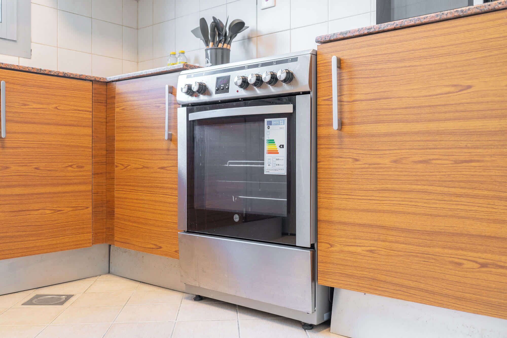 Una cocina con armarios de madera, horno de acero inoxidable y suelo de baldosas.