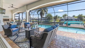 A spacious indoor area with a large window overlooking a swimming pool, wicker furniture, and ceiling fans. - • Sleeps 6 | 3 bedrooms |3 baths - Stars Vacation Rentals (Cape Coral)