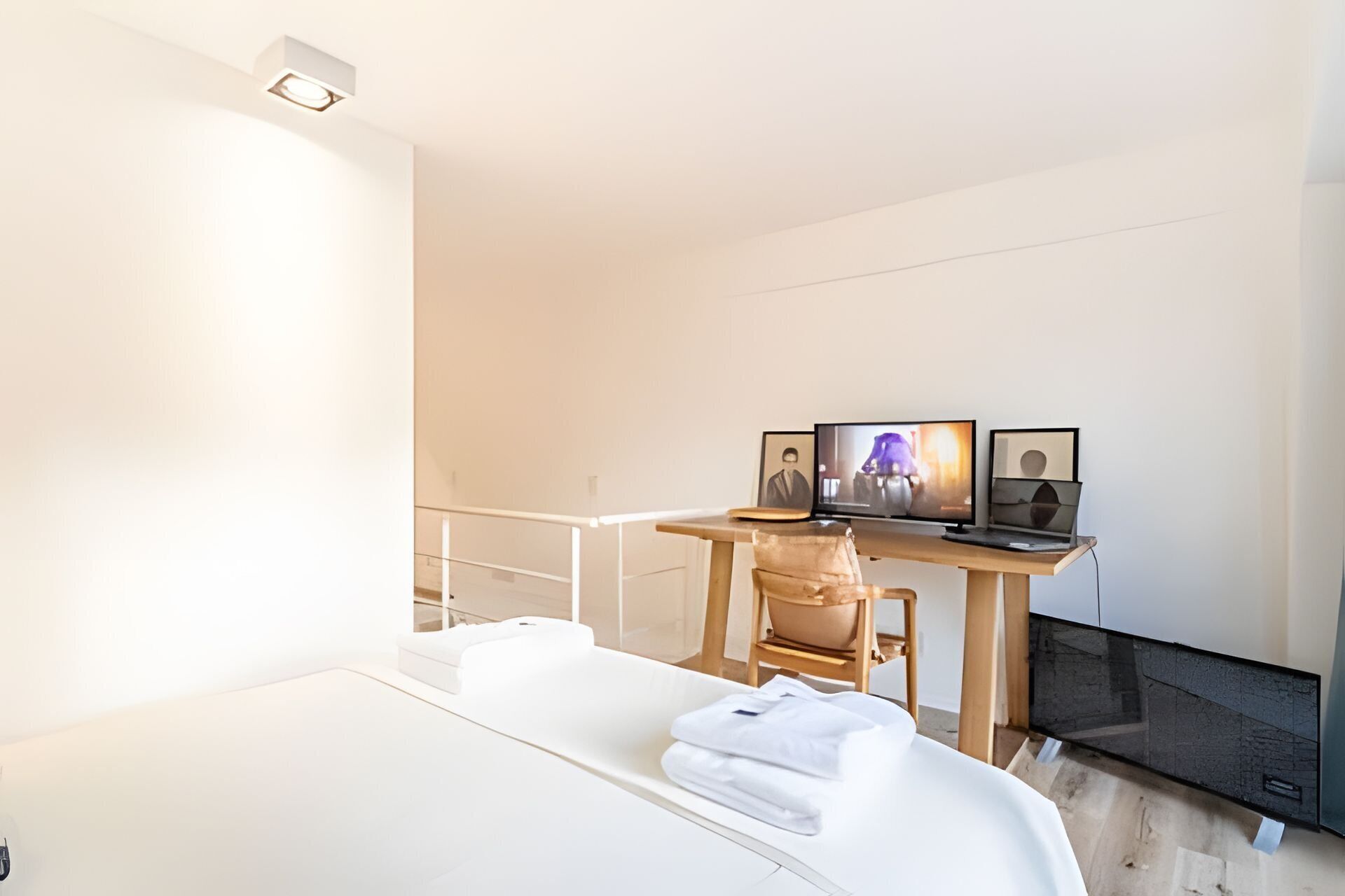 Ein modernes Hotelzimmer mit einem Bett, einem Schreibtisch mit Laptop und Fernseher sowie einem Sessel.