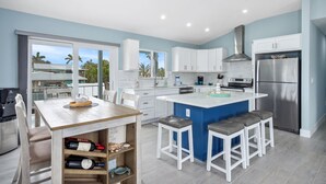 Une cuisine moderne avec des meubles blancs, un réfrigérateur en acier inoxydable et un grand îlot central doté de tabourets de bar.