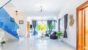 Een moderne woonkamer met een bank, salontafel en potplanten. Een trap met blauwe accenten leidt naar een ander niveau.