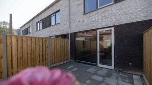 Et moderne hus med to etager, murstensfacade, store vinduer og en skydedør, der fører til en patio.