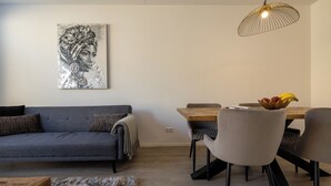 En moderne stue med en grå sofa, et træspisebord med stole, en hængende lampe og et billede på væggen.