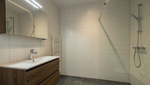 Et moderne badeværelse med et trækommode, en hvid vask og en bruseniche med håndbruser.