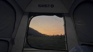 A tent with a clear view of a sunset over a grassy field.