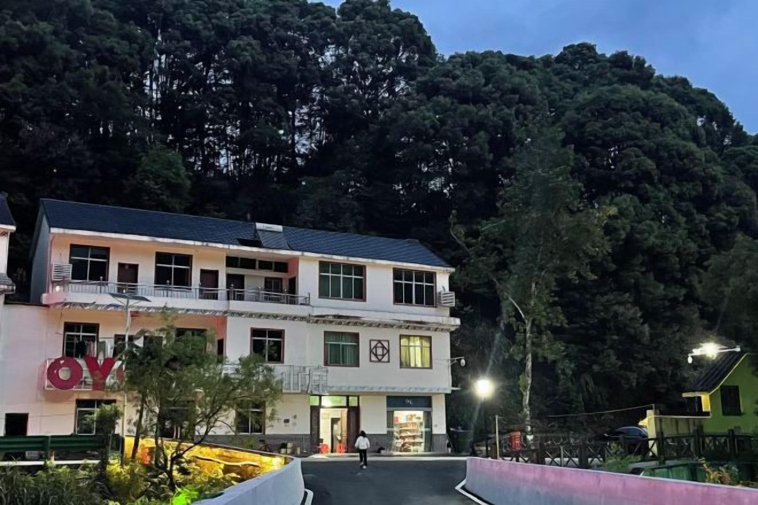Un edificio de dos plantas con balcón, rodeado de follaje y árboles.