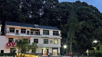 Un edificio de dos plantas con balcón, rodeado de follaje y árboles.