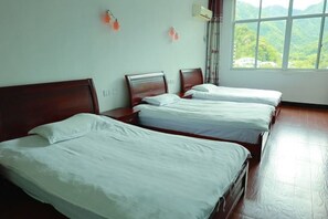 Une chambre d’hôtel avec trois lits, une grande fenêtre donnant sur les montagnes et un climatiseur fixé au mur.