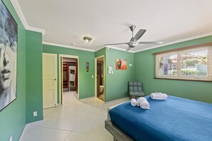 A bedroom with a bed, a ceiling fan, a window with blinds, a door leading to a bathroom, and a green wall.