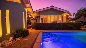 A modern hotel with a swimming pool, a well-maintained garden, and a thatched-roof structure.