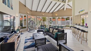 Amplia sala de estar con techo alto, un conjunto de sofás, una silla colgante, una zona de bar y ventanas grandes que ofrecen vistas al exterior.