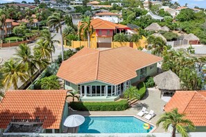 A large house with a swimming pool, surrounded by palm trees and other houses.