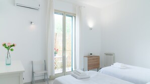 Une chambre d’hôtel propre et blanche, avec deux lits, un bureau, une chaise et une fenêtre avec des rideaux.