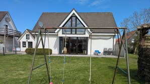 Ein Wohnhaus mit gepflegtem Rasen, einer Schaukel und einem Dach mit Ziegeln sowie großen Fenstern.