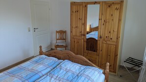 A bedroom with a wooden bed, a wooden wardrobe, a chair, and a drying rack.