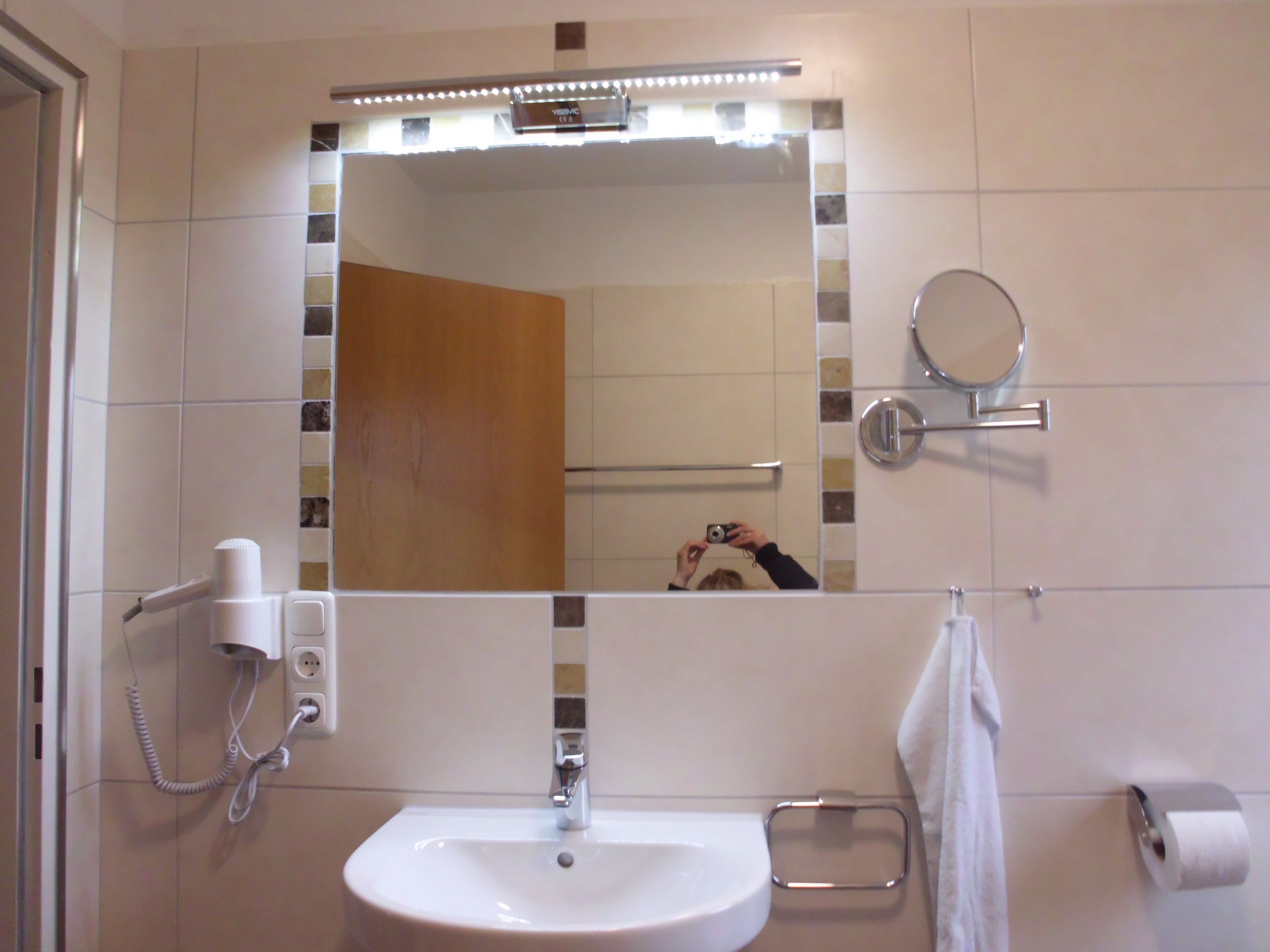 Et badeværelse med en hvid vask, et spejl, en håndklædestang, en toiletpapirholder og en hårtørrer.