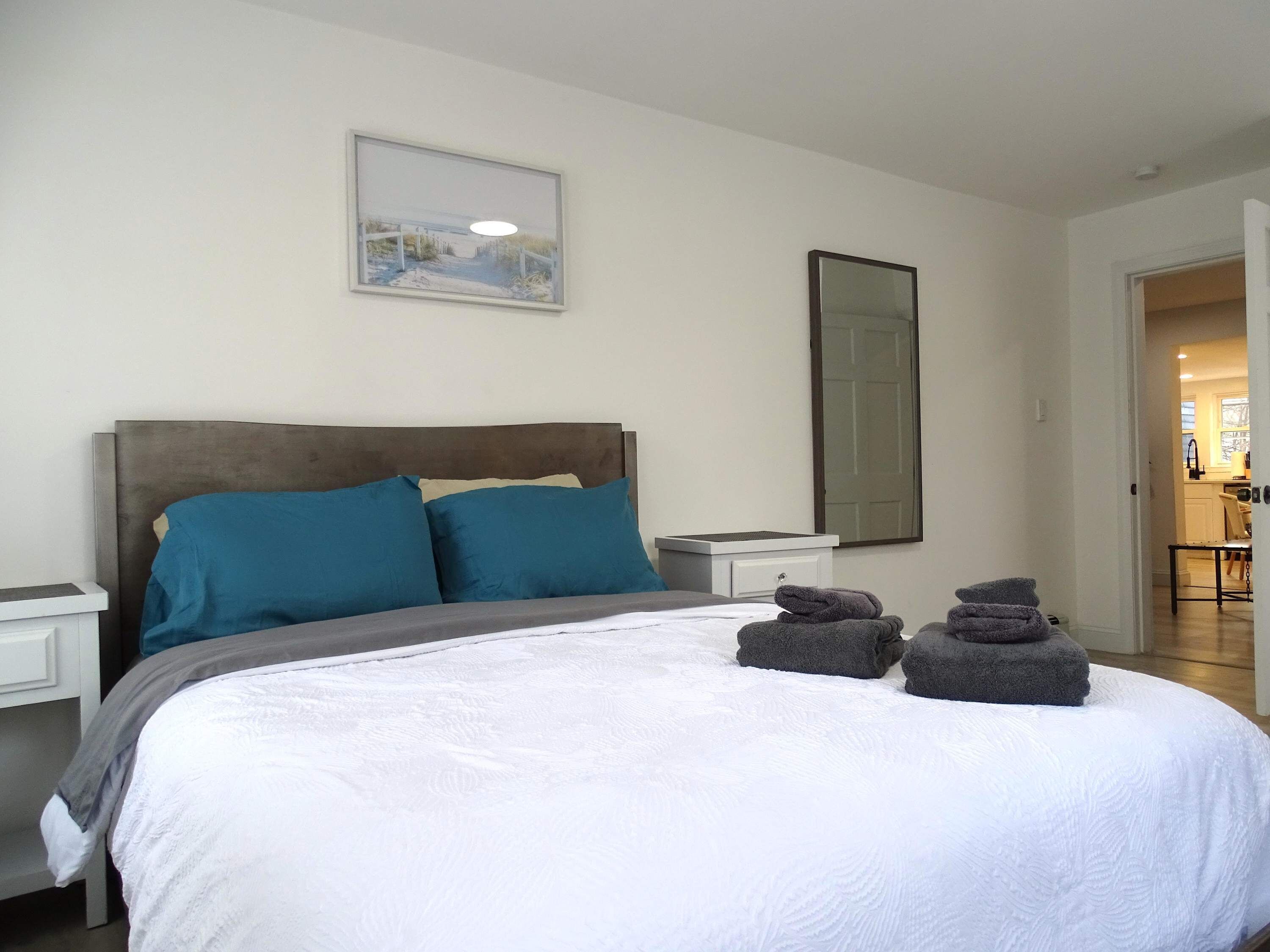 A neatly made bed with blue and gray pillows, a white comforter, and a few folded towels on the bed.