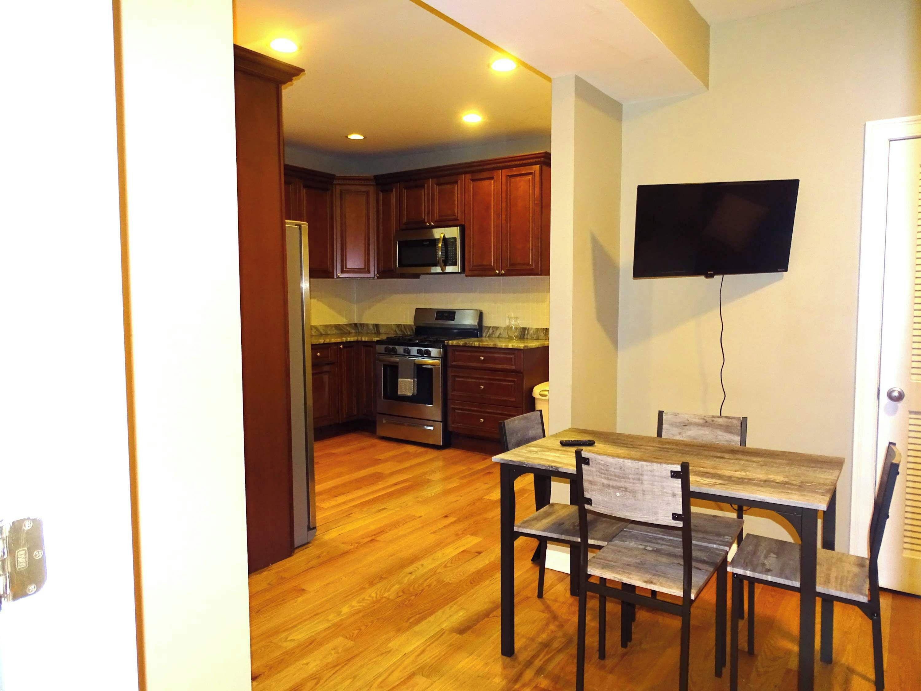 Una cocina con armarios de madera, una estufa de acero inoxidable y un microondas. Hay una mesa de comedor con sillas y un televisor de pantalla plana montado en la pared.
