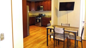A kitchen with wooden cabinets, a stainless steel stove, and a microwave. There is a dining table with chairs and a flat-screen TV mounted on the wall. - Beautiful 2 Bed Apt, Minutes from Encore (Everett)