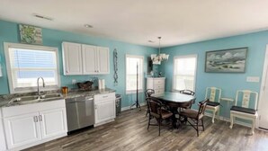 A kitchen with white cabinets, a dishwasher, a dining table with chairs, and a chandelier. - 3-bedroom villa in charming North Topsail Beach with WiFi, AC  Ocean front view (North Topsail Beach)