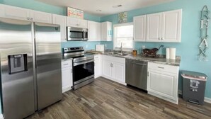 A modern kitchen with white cabinets, stainless steel appliances, and a wooden floor. - 3-bedroom villa in charming North Topsail Beach with WiFi, AC  Ocean front view (North Topsail Beach)