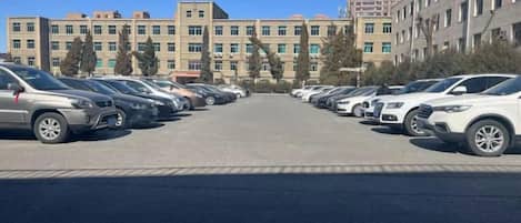 A parking lot with multiple rows of parked cars and a building with multiple floors in the background.