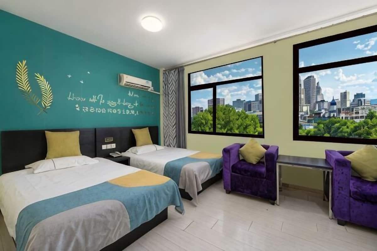 A hotel room with two beds, a bench, purple chairs, a city view, and a teal wall with text.